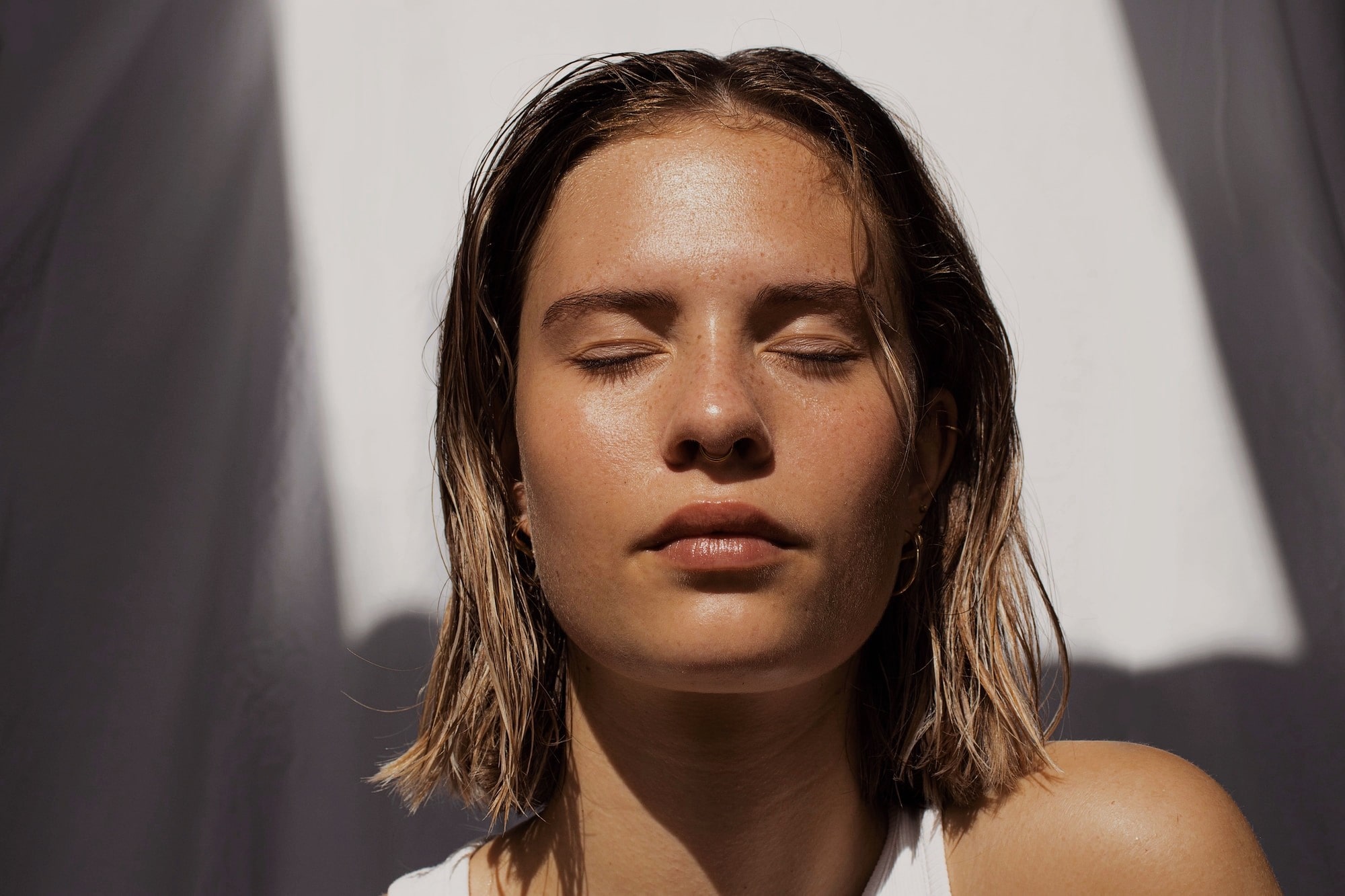 A fresh faced woman with her eyes closed. She has the sun beeming on her face.